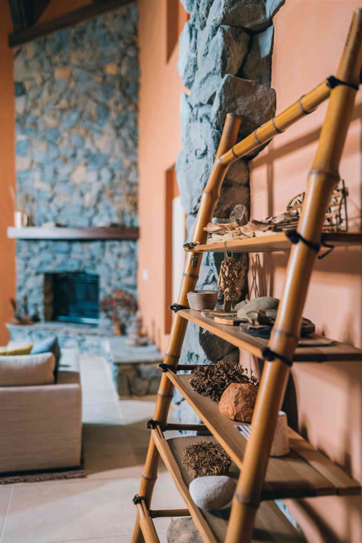 A close-up of a Japandi living room wall featuring a portion of a stone accent wall next to a clay-colored painted wall. A bamboo ladder shelf in the foreground to showcase the use of natural materials in furniture and decor.