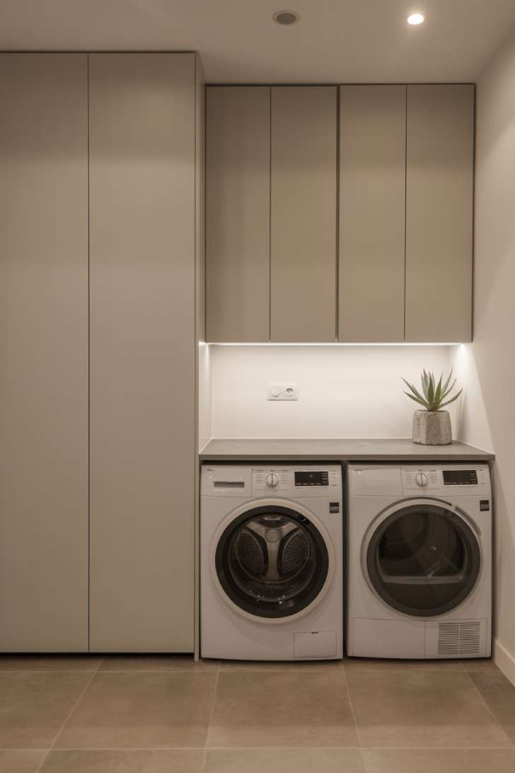 Floor-to-ceiling handleless white cabinets surrounding built-in laundry machines with a clear grey quartz countertop