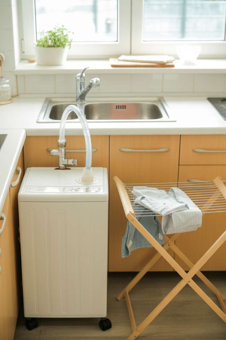 Portable washing machine connected to a kitchen sink faucet with a small foldable drying rack beside it
