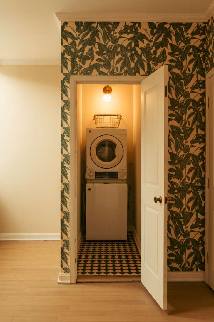 Laundry closet with checkered floor tile and bold botanical wallpaper surrounding stackable machines