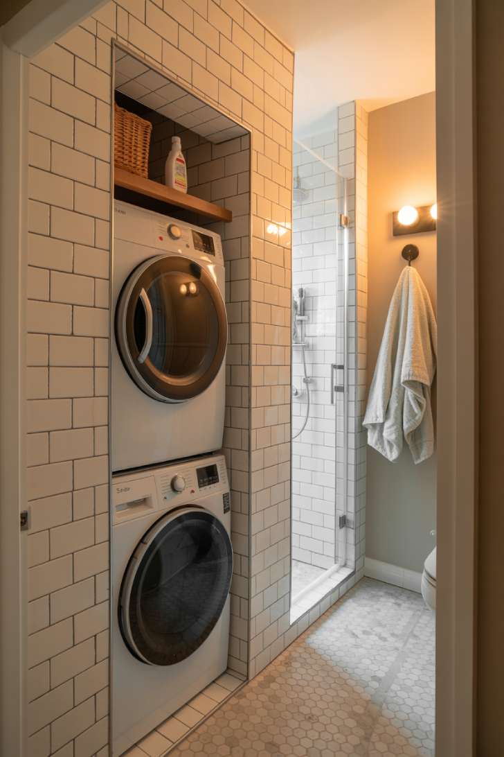 Stackable washer and dryer installed in a tiled bathroom alcove beside a glass shower