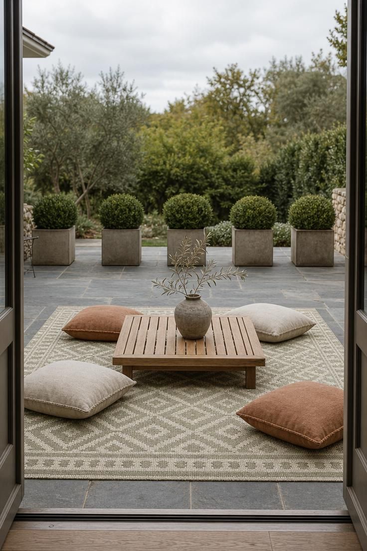 Flat-weave polypropylene rug in sage and ivory on a bluestone patio with a low teak coffee table and linen floor cushions under overcast morning light.