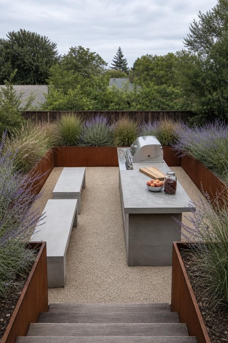 Sunken gravel pad outdoor kitchen bordered by Corten steel planter walls with ornamental grasses under overcast morning light