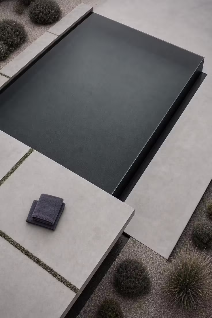15 Backyard Pool Designs That Bring Resort Comfort Home 12 Overhead view of a dark quartz vanishing-edge pool with cantilevered concrete deck in soft diffused light.