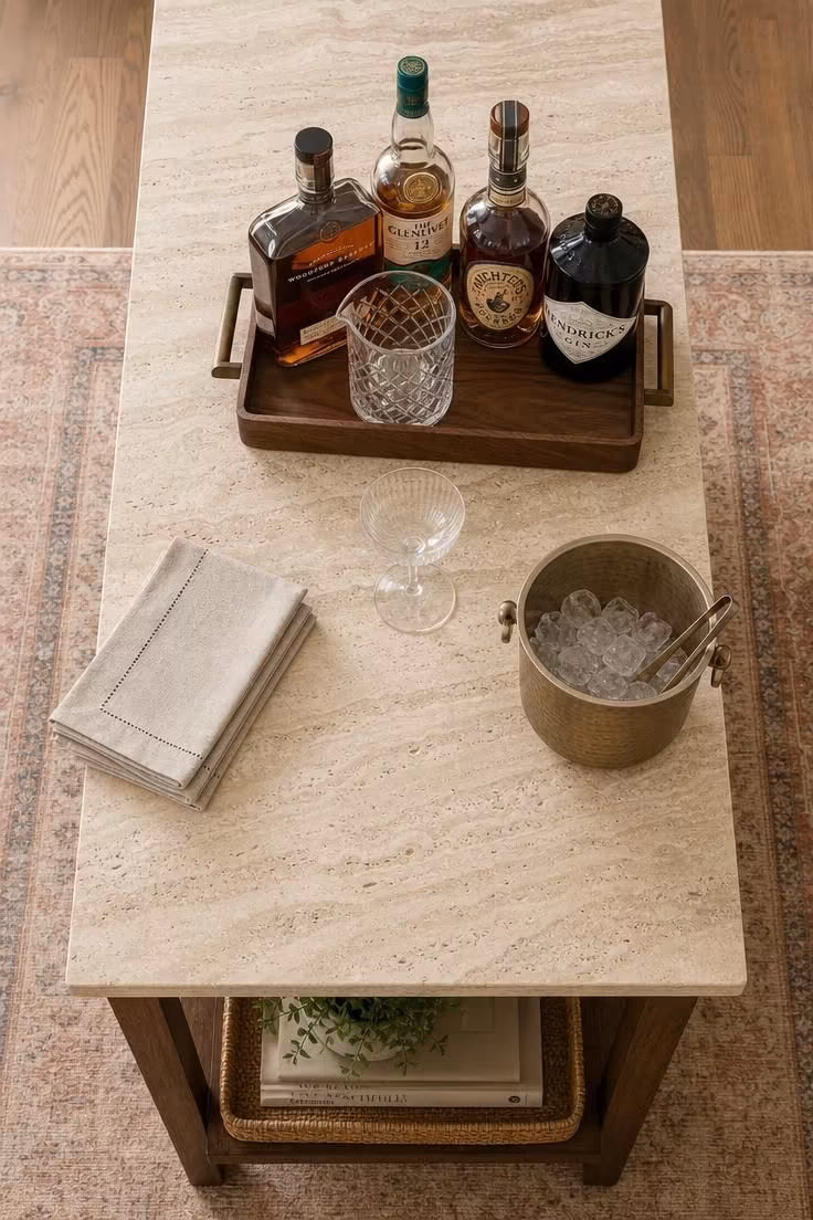 11 Cozy Bar Ideas for Home Living Rooms You'll Love 9 Overhead view of a travertine-topped console table styled with a tray of spirits, linen napkins, and an ice bucket