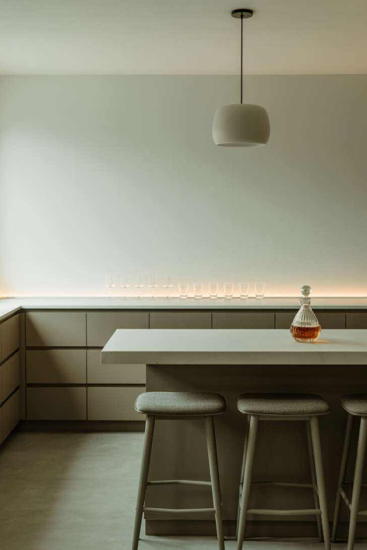 A sleek modern basement bar with a white quartz waterfall countertop, handleless charcoal cabinetry, and a single white ceramic pendant