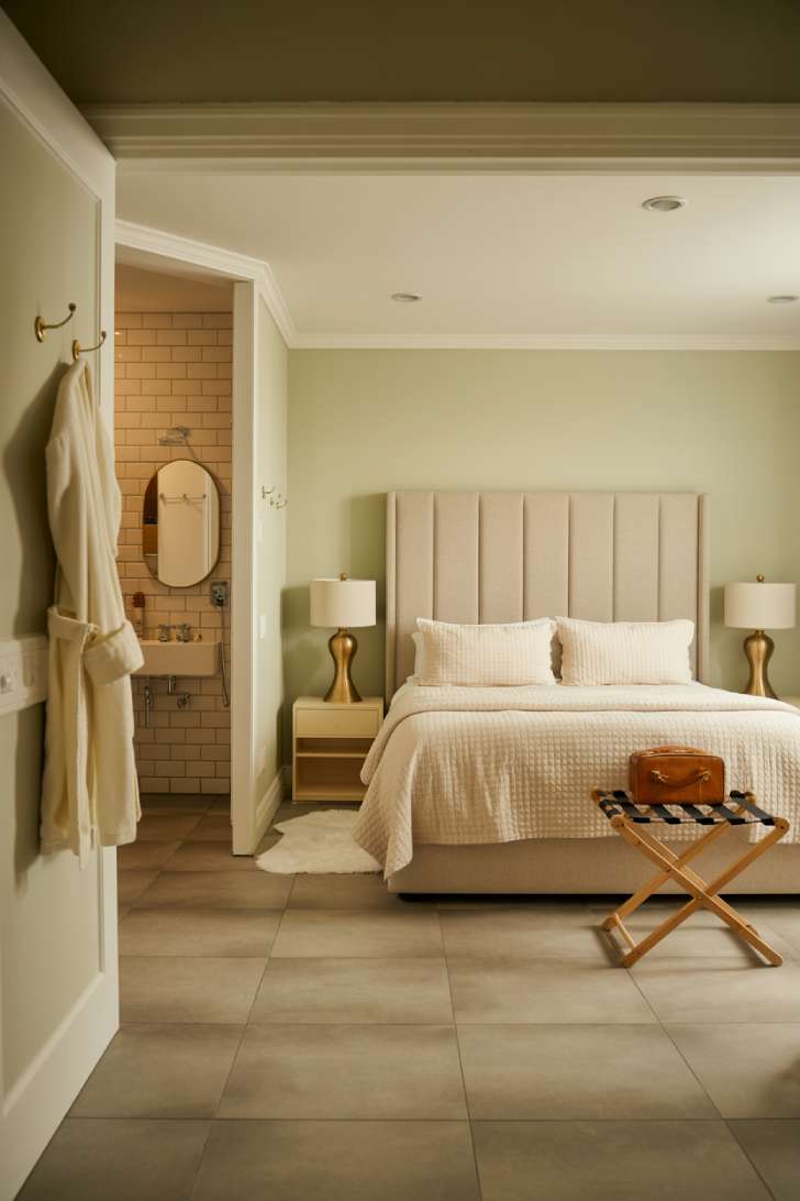 Luxury basement guest suite with sage green walls, king bed, brass accents, and a glimpse of the en-suite bathroom through an open doorway