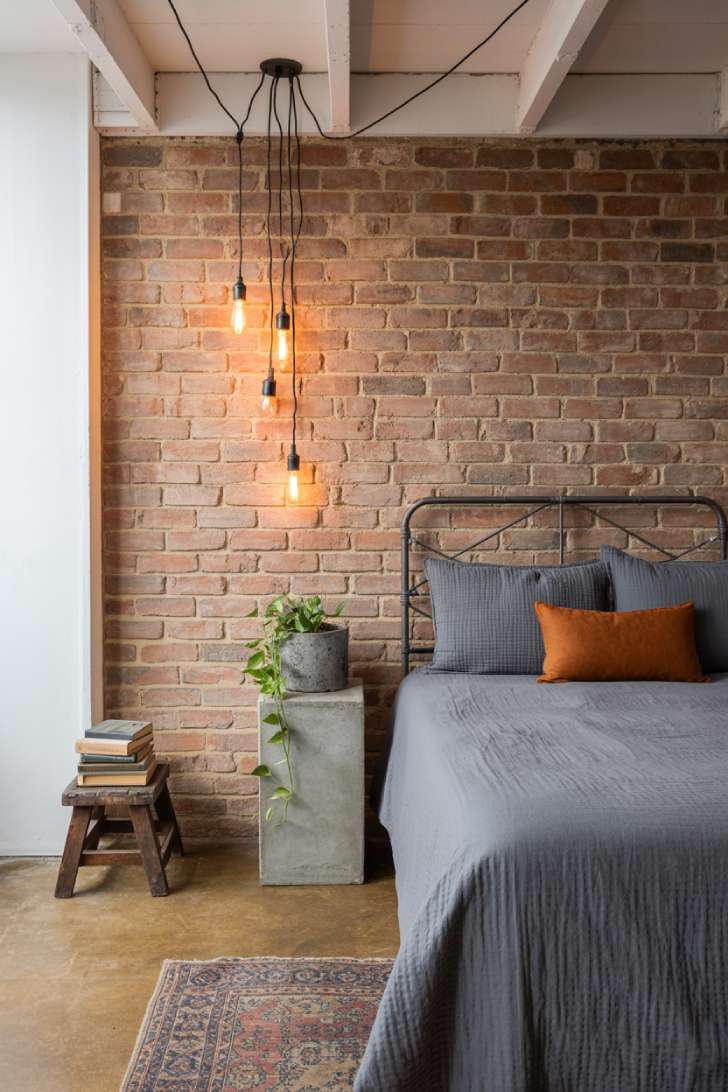 Industrial basement bedroom with exposed brick wall, black iron bed frame, Edison pendants, and vintage Persian runner