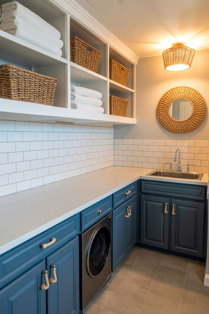 Coastal basement laundry room with navy blue cabinets, rope hardware, white subway tile, and natural seagrass baskets
