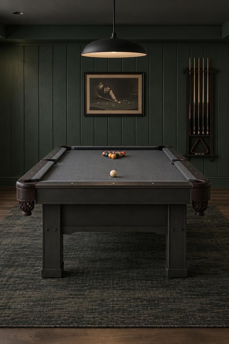 Game room setup with a deep green board and batten wall, a gunmetal pool table on a charcoal and green flatweave rug, a matte black pendant, and a framed vintage pool print under moody low light.