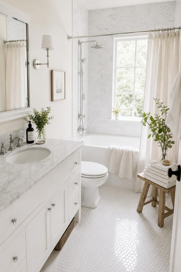 Bright all-white bathroom layered with marble, linen, and polished chrome.