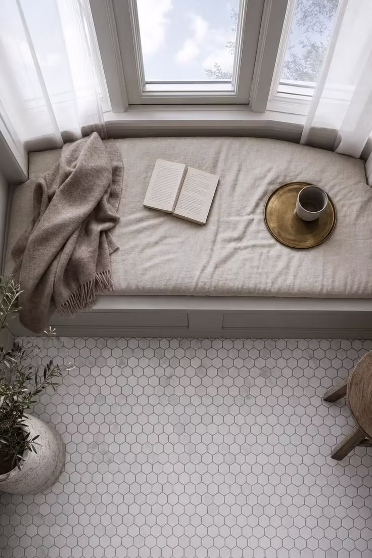 Overhead view of a bay window reading nook with white marble hexagon floor tiles and a natural linen bench cushion.