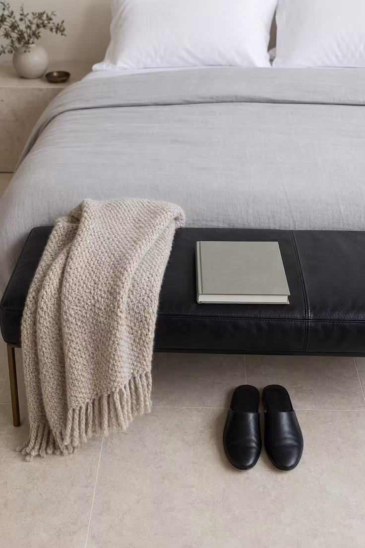 13 Cozy Bedroom Ideas With Black Furniture for Any Style 12 Black leather bench with woven wool throw at the foot of a bed on pale limestone tile in cool overcast light