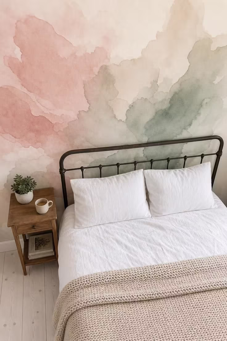 9 Bedroom Wall Decorations That Instantly Make a Plain Room Feel Custom 5 An overhead view of a bed against a wall covered in large-scale abstract watercolor wallpaper in blush, sage, and cream, with soft diffused light and white linen bedding.