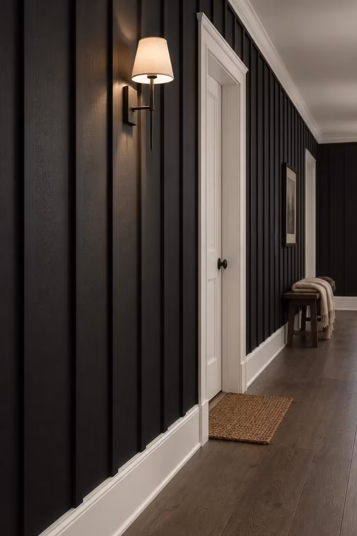 13 Warm Black and White Hallway Ideas for a Bold Entry 2 A hallway wall paneled in matte black board-and-batten with crisp white baseboards and door casings, lit softly by a wall sconce.