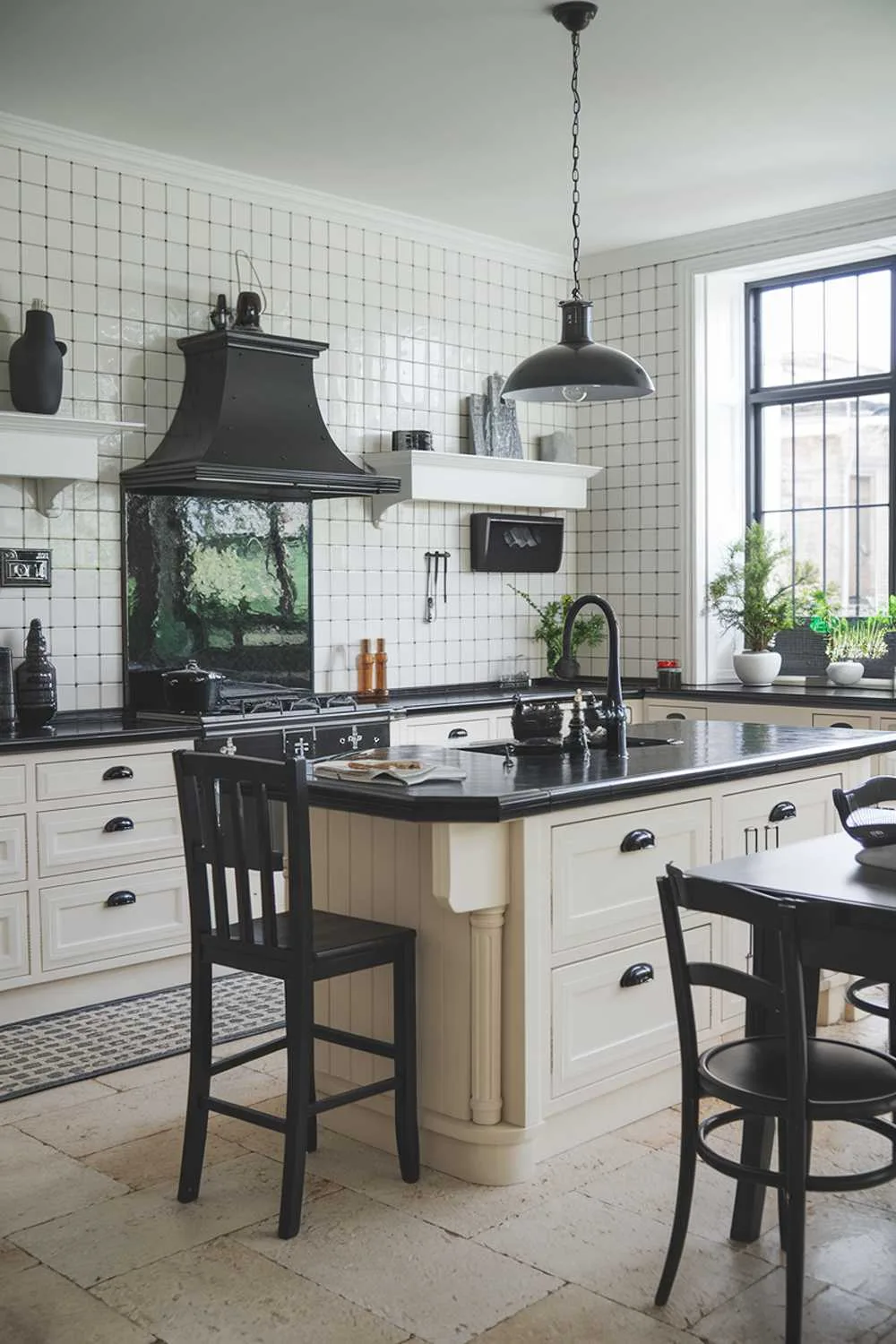 23 Stunning Black and White Kitchen Ideas for Timeless Style 8 A white kitchen with black accents, featuring a large island with a black countertop and a black pendant light hanging above it. There is a black faucet and a black stove hood over the island. The cabinets have black handles and the backsplash has a black and white tile pattern. There is a black chair at the island and a black table with two chairs near the window. The floor is made of beige tiles. There are potted plants near the window and on the countertop. The walls have a few decorative items, including a black vase and a white vase with a black base.