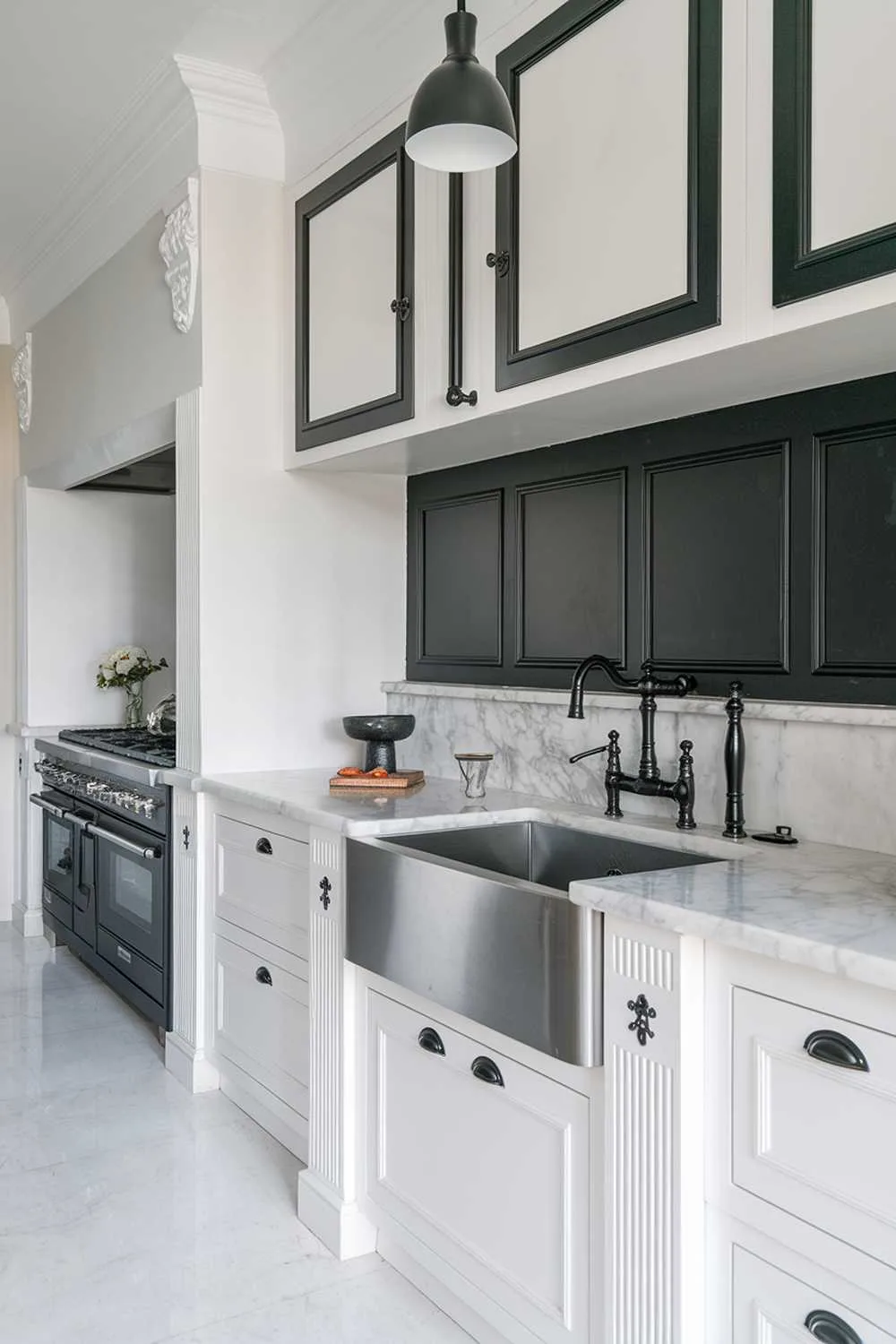 23 Stunning Black and White Kitchen Ideas for Timeless Style 12 A white kitchen with black accents. The kitchen has a marble countertop, a stainless steel sink, and a black faucet. There is a white cabinet with black accents above the sink. The wall behind the cabinet has a black accent panel. The floor is made of white tiles. There is a black pendant light hanging above the sink.