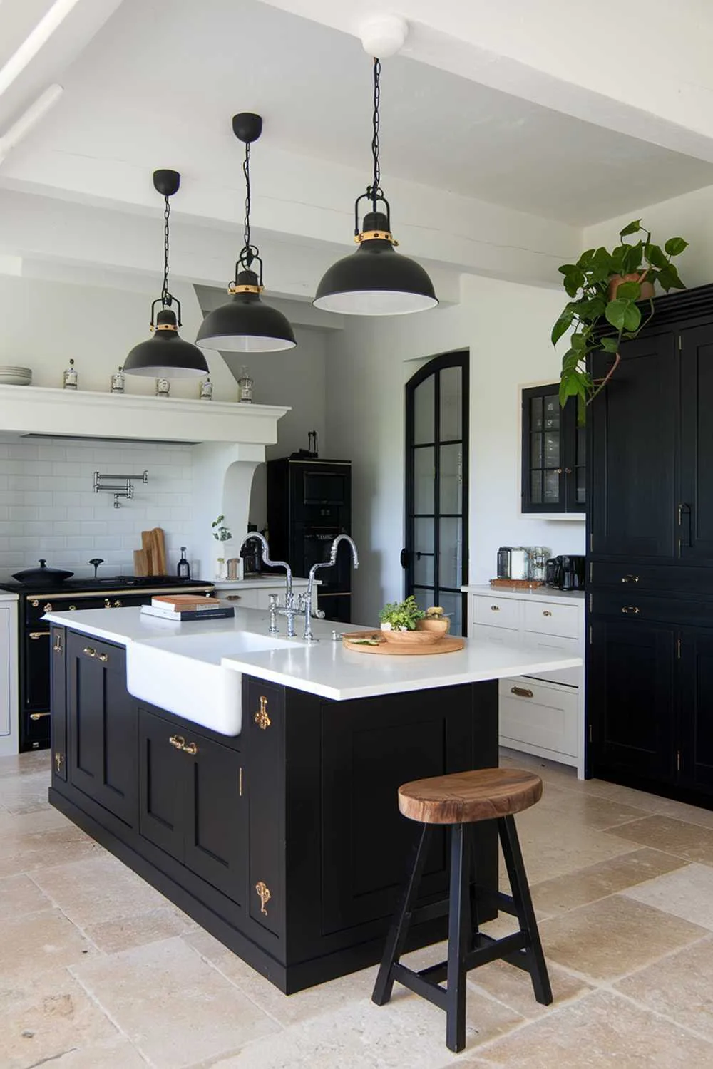 23 Stunning Black and White Kitchen Ideas for Timeless Style 14 A white kitchen with black accents, including a black island with a white countertop, black pendant lights, and black cabinetry. The kitchen has a farmhouse sink, a double oven, and a hood over the stove. There is a wooden stool near the island and a potted plant near the black cabinet. The floor is made of beige tiles.