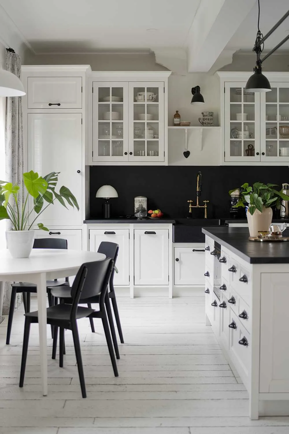 23 Stunning Black and White Kitchen Ideas for Timeless Style 15 A white kitchen with black accents. The kitchen has a white island with a black counter and a black sink. There are white cabinets with black handles and a black backsplash. There is a white table with black chairs. The floor is made of white tiles. There are potted plants and a lamp on the counter.