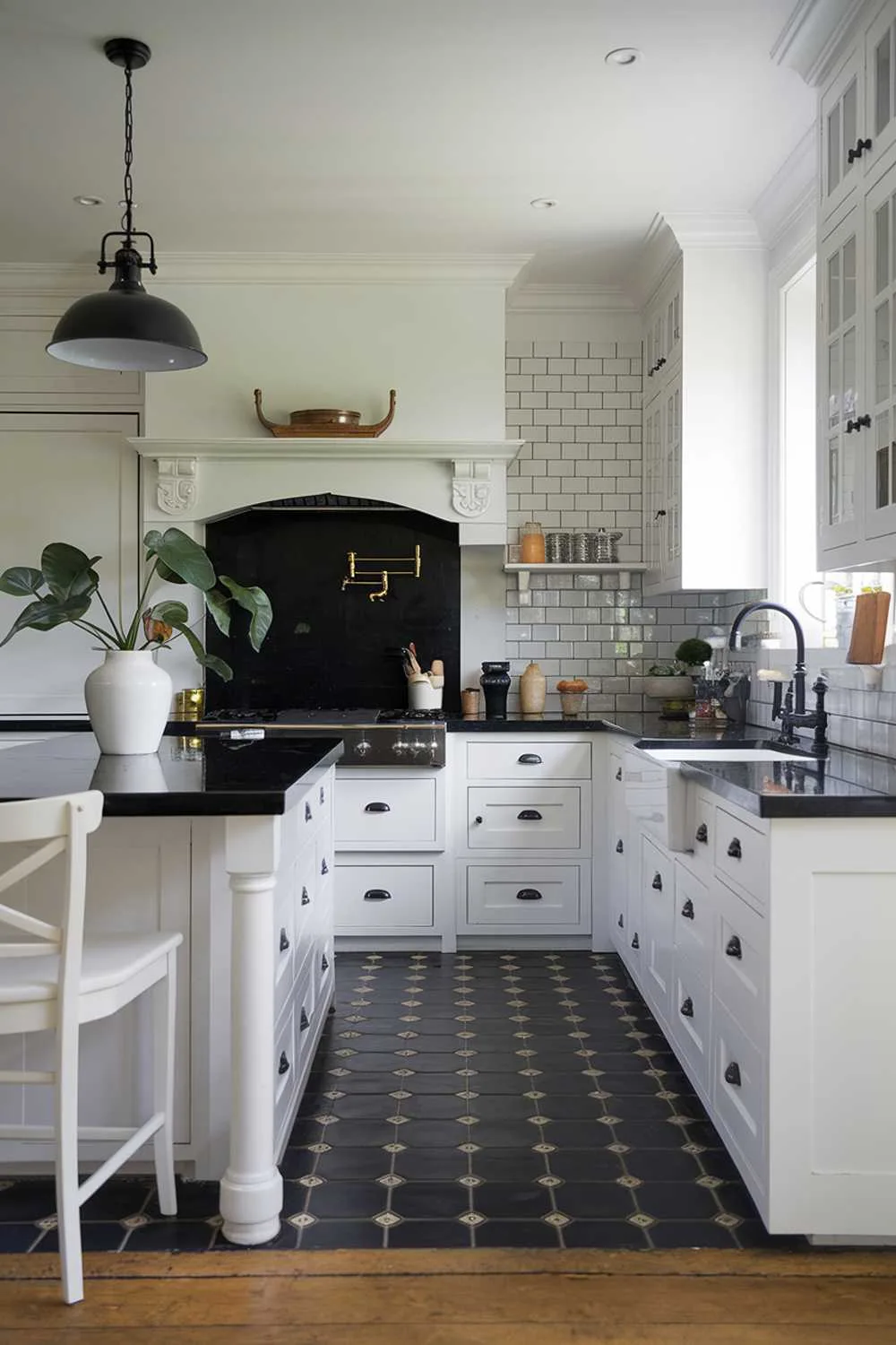 23 Stunning Black and White Kitchen Ideas for Timeless Style 17 A cozy white kitchen with black accents. The kitchen has a white island with a black countertop, white cabinets, and a black backsplash. There is a white sink with a black faucet. The floor is made of black and white tiles. A black pendant light hangs over the island. A white chair is placed near the island. A potted plant is placed on the countertop.