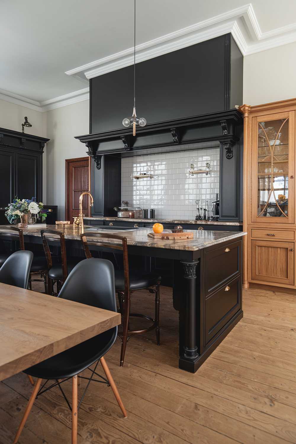 A wide shot of a highly detailed elegant black and wood kitchen design. The kitchen has a black island with a marble countertop and a wood dining table. There are black chairs with wooden legs near the island. The backsplash behind the black island is made of white tiles. There's a black cabinet on the left wall and a wood cabinet on the right wall. The flooring is made of wood.