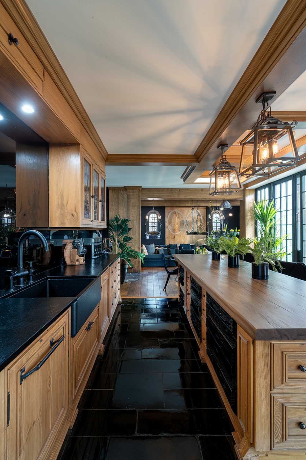 A black and wood kitchen design. The kitchen has a black countertop and backsplash, with a wooden cabinet and island. There is a black sink and faucet. The wooden elements have a natural tone. There are potted plants on the wooden countertop. The floor is made of black tiles. The lighting is bright. The background reveals a living area with a sofa and a plant.