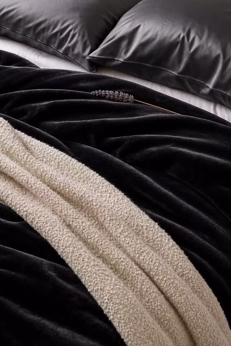 13 Moody Black Nouveau Bedroom Ideas Worth Trying Now 7 Close-up of black velvet bedding layered with ivory boucle throws and charcoal silk pillowcases in soft diffused daylight.