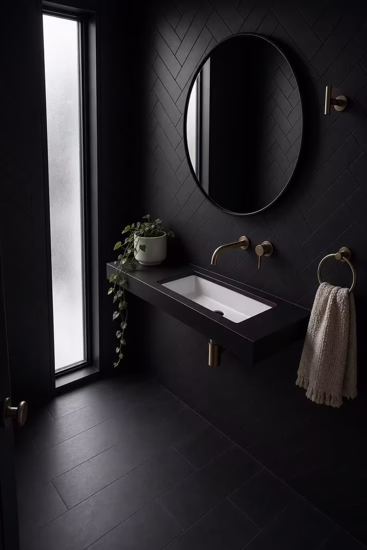 11 Bold Black Powder Room Ideas for a Moody Retreat 2 Matte black herringbone tile powder room with raw brass towel ring and white undermount sink in cool overcast light