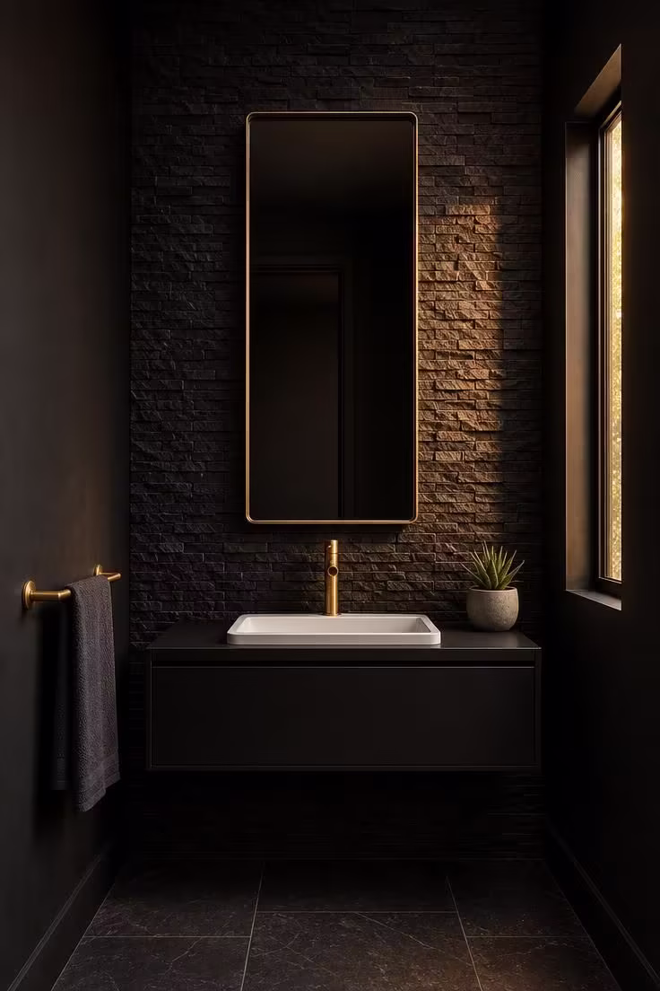 11 Bold Black Powder Room Ideas for a Moody Retreat 6 Jet black stacked stone accent wall with floating steel vanity and brass faucet in warm golden light