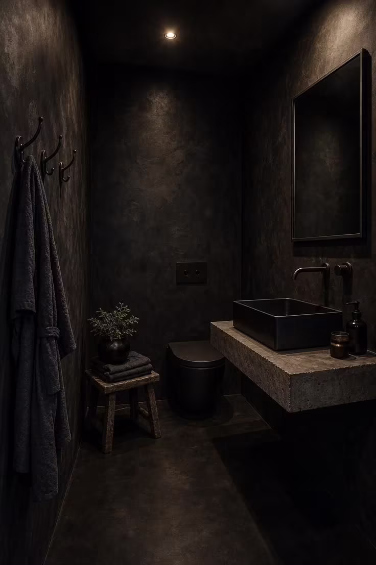 11 Bold Black Powder Room Ideas for a Moody Retreat 10 Black microcement powder room with teak stool and iron hooks in moody low ambient lighting