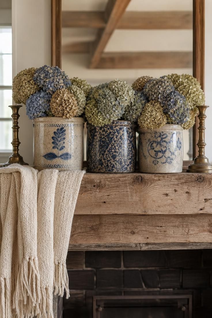 11 Cozy Blue and White Fall Decor Ideas for Warmth 2 Three cobalt and cream spongeware crocks filled with dried hydrangeas on a reclaimed pine mantel with a cream wool throw and brass candlesticks.