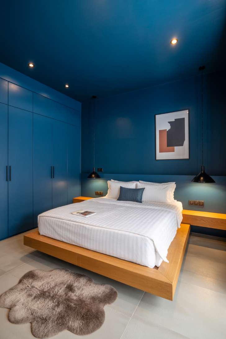 15 Charming Blue Guest Bedroom Ideas for Warm Welcomes 14 Sleek modern guest bedroom with midnight blue matte walls and ceiling, floating oak platform bed, white bedding, geometric art print, black pendant lamp, and sheepskin rug