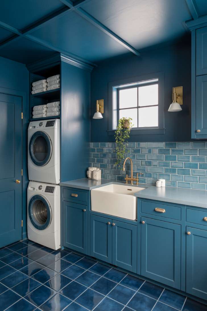 Monochromatic blue laundry room with varying tones of blue on walls, cabinets, and floor tiles, accented with brushed gold hardware