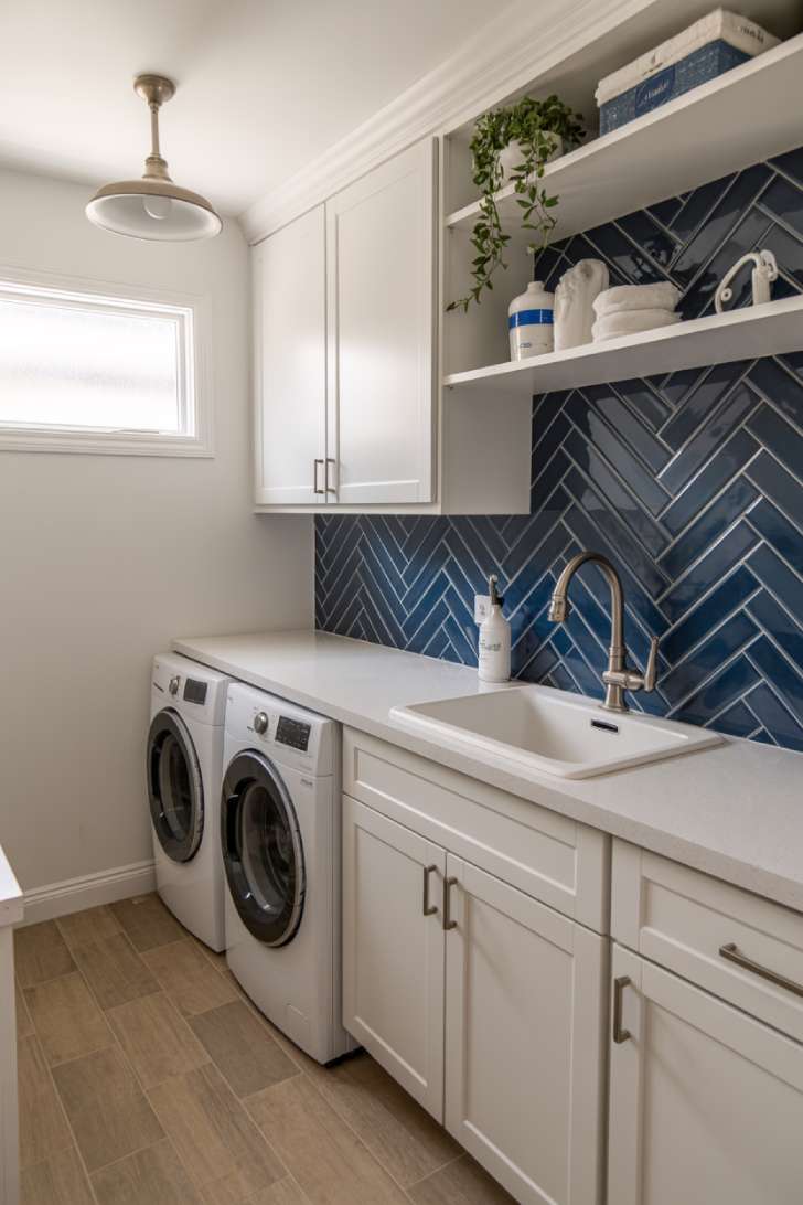 Navy blue herringbone tile backsplash in a compact white laundry room with warm wood floor tiles