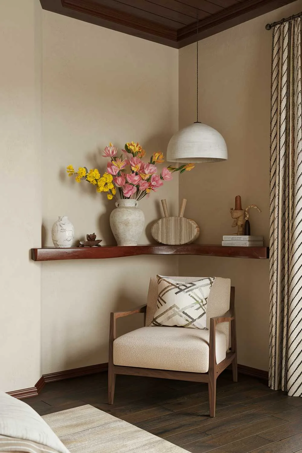 A boho bedroom decor. The room has a beige wall, a wooden ceiling, and a dark wooden floor. There is a beige chair with a wooden frame in the corner. There is a wooden shelf above the chair. On the shelf, there is a white vase with pink and yellow flowers, a white lampshade, a beige cushion, and a few decorative items. The room has soft lighting.