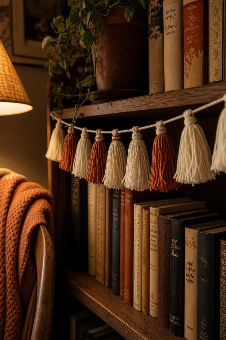 Cream and rust tasseled cotton garland strung across a book-filled reading corner shelf in soft lamp light.