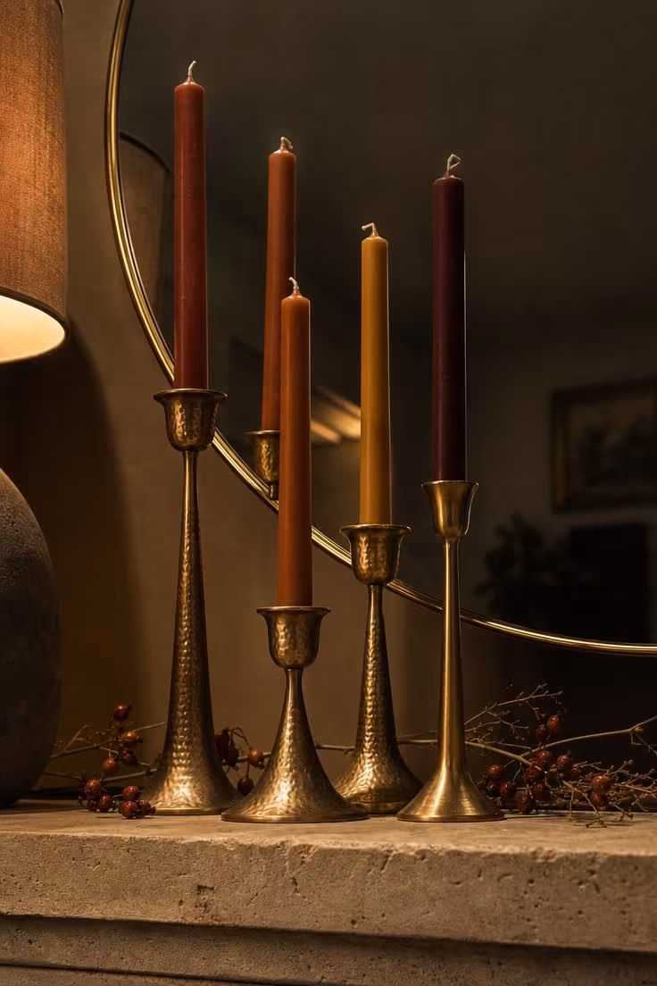 15 Classy Fall Decor Ideas That Feel Collected and Warm 4 Terracotta and cinnamon taper candles in hammered brass holders arranged on a limestone mantel