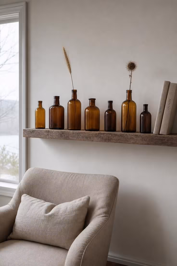 15 Classy Fall Decor Ideas That Feel Collected and Warm 8 Vintage amber glass bottles in varying heights on a floating shelf with dried wheat and thistle stems