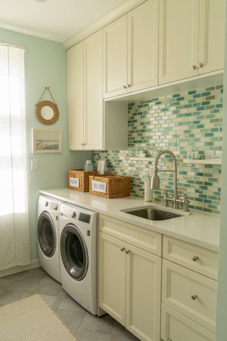 Sea green mosaic tile backsplash coastal laundry room with white shaker cabinets and rattan mirror