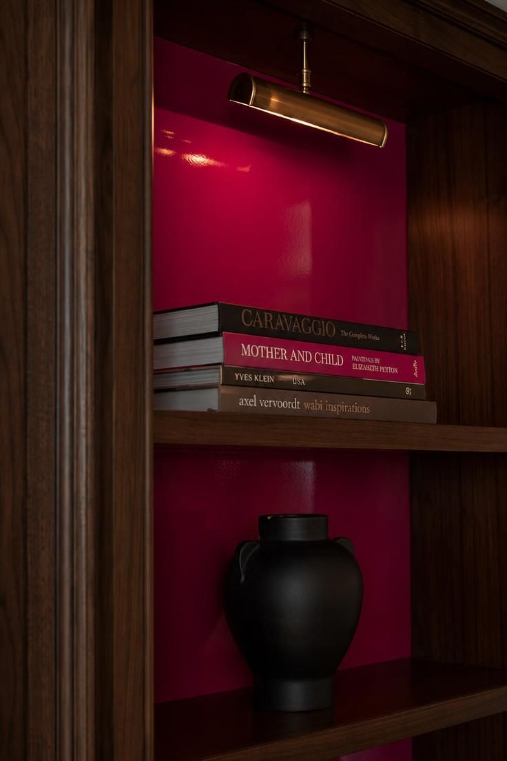 14 Colorful Eclectic Home Ideas for a Joyful Space 2 Walnut bookcase with a high-gloss magenta interior glowing under a brass picture light.