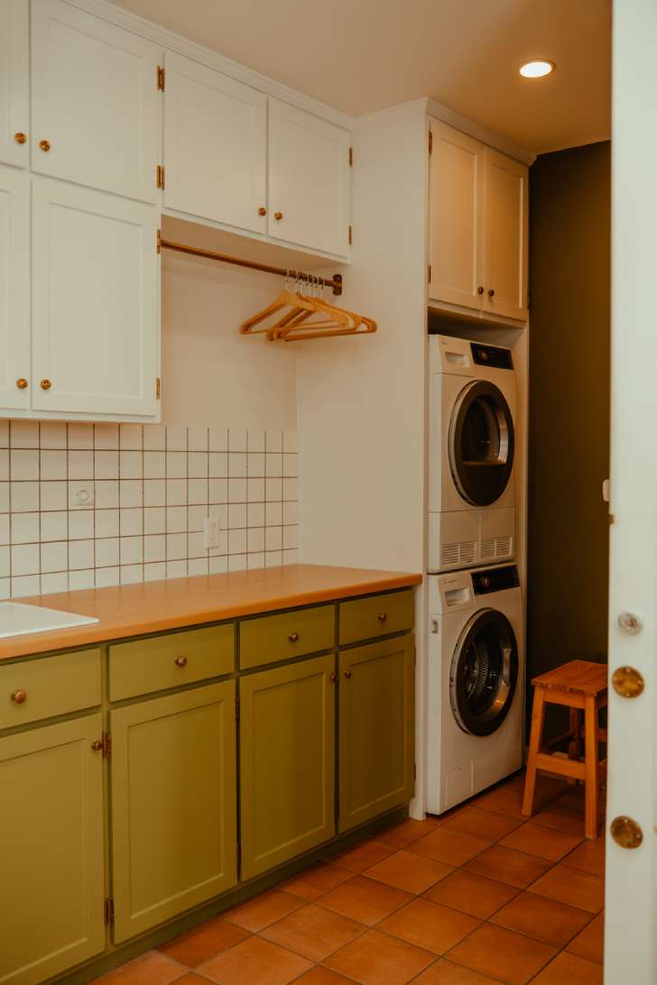 11 Dreamy Colorful Laundry Room Ideas You Need to See 9 A laundry room with white upper cabinets and olive green lower cabinets, terracotta floor tile, and a warm wood countertop
