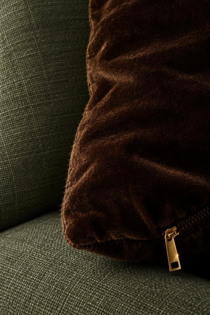 The Bold Colors That Go with Sage Green for a Room with Personality 4 A close-up of a chocolate brown velvet cushion against sage green upholstery with a brass zip pull.