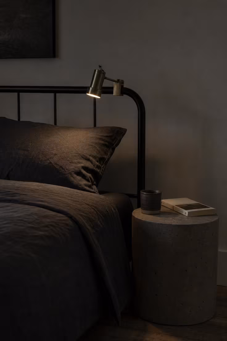 11 Cool Bedroom Ideas for Men Craving a Moodier Retreat 7 Poured-concrete side table beside a low iron bed frame in dim, moody light.