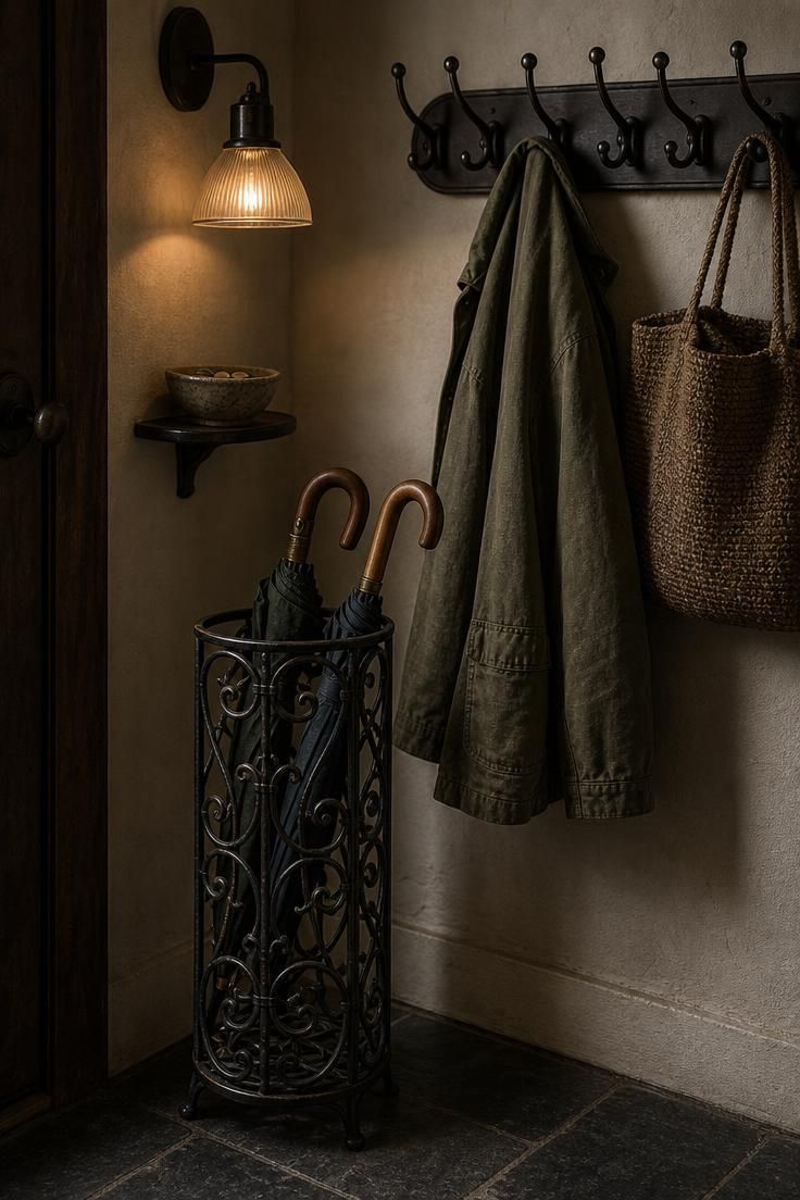 26 Charming Cottage Entryway Ideas for a Cozy Welcome 18 Wrought-iron umbrella stand and oil-rubbed bronze coat rack in a moody cottage entryway corner with amber sconce light