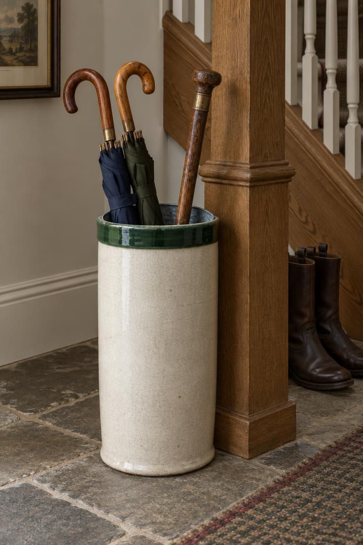 11 Warm Country Style Hallway Ideas for a Welcoming Home 9 Cream ceramic umbrella stand with a green rim holding wooden-handled umbrellas and a walking stick, with a galvanized bucket liner visible inside.