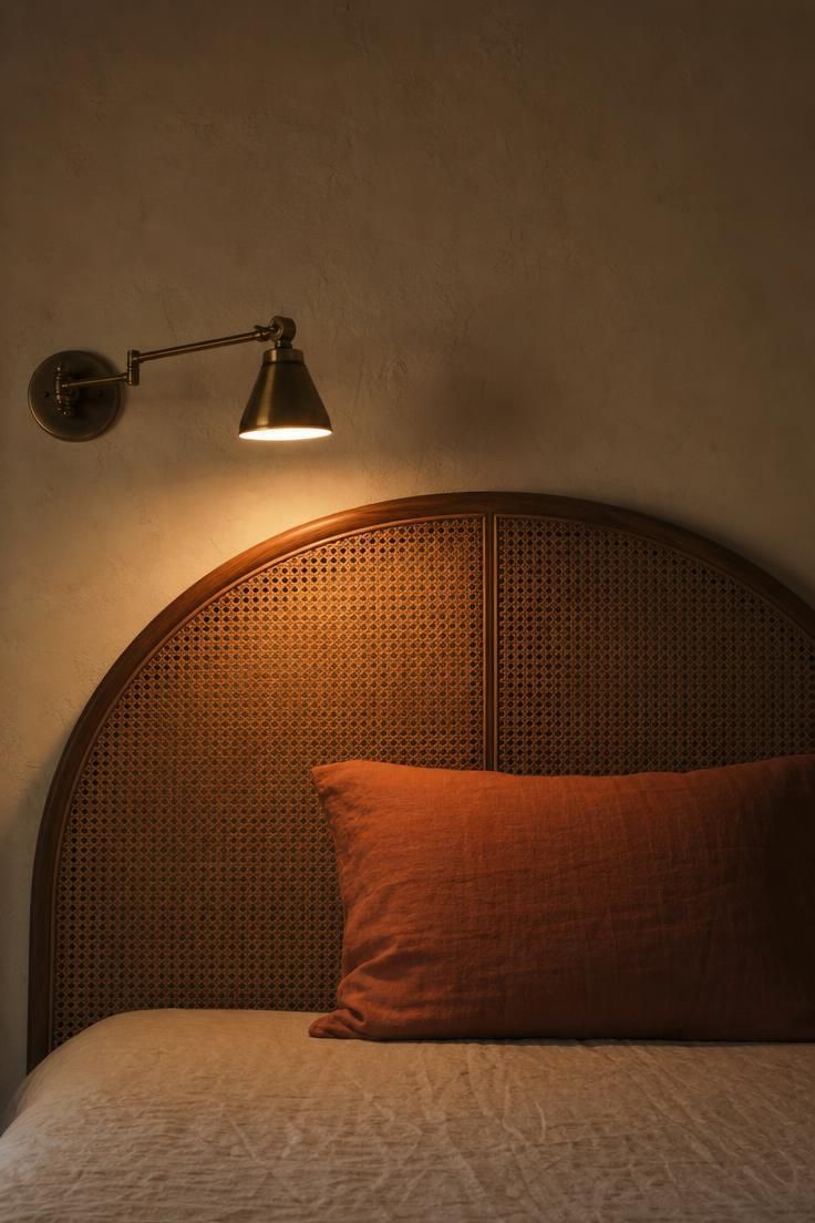 Arched cane headboard against a warm plaster wall with a single brass sconce casting amber light.