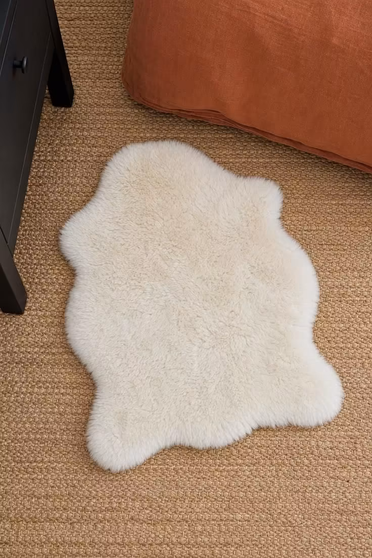 11 Warm & Inviting Cozy Fall Bedroom Retreat Tips Now 7 A small ivory faux shearling layered over a flat-woven jute rug at the side of a bed with a rust duvet.