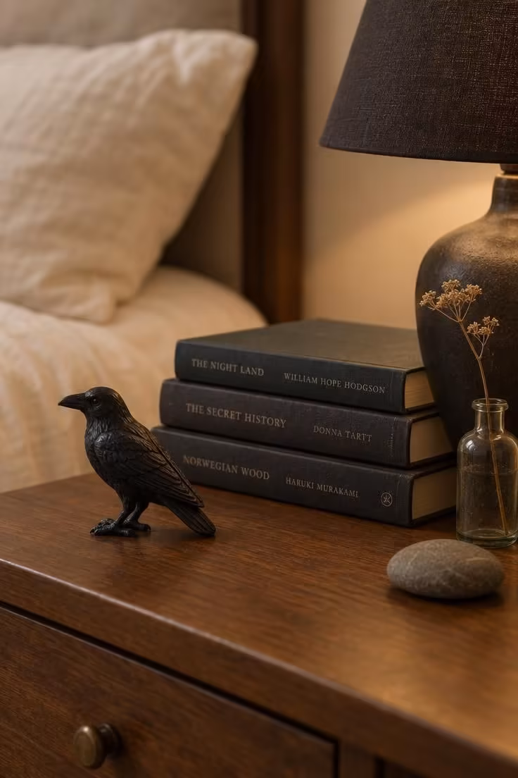 11 Cozy Halloween Bedroom Ideas for Calm Autumn Nights 6 Single black raven figurine on a nightstand beside a small lamp and a short stack of books.