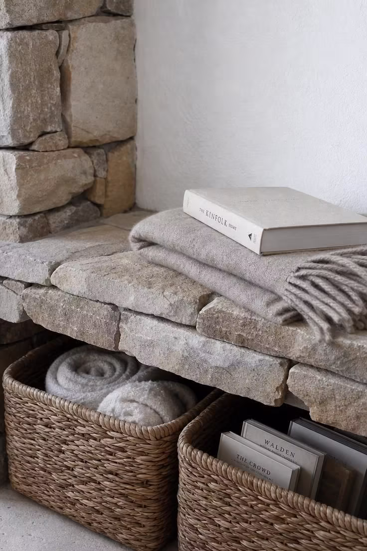 15 Cozy Reading Nook Ideas That Feel Like a Warm Hug 13 Close-up of a stacked stone ledge with a wool throw and book, woven rattan baskets below, in cool flat north-facing light.