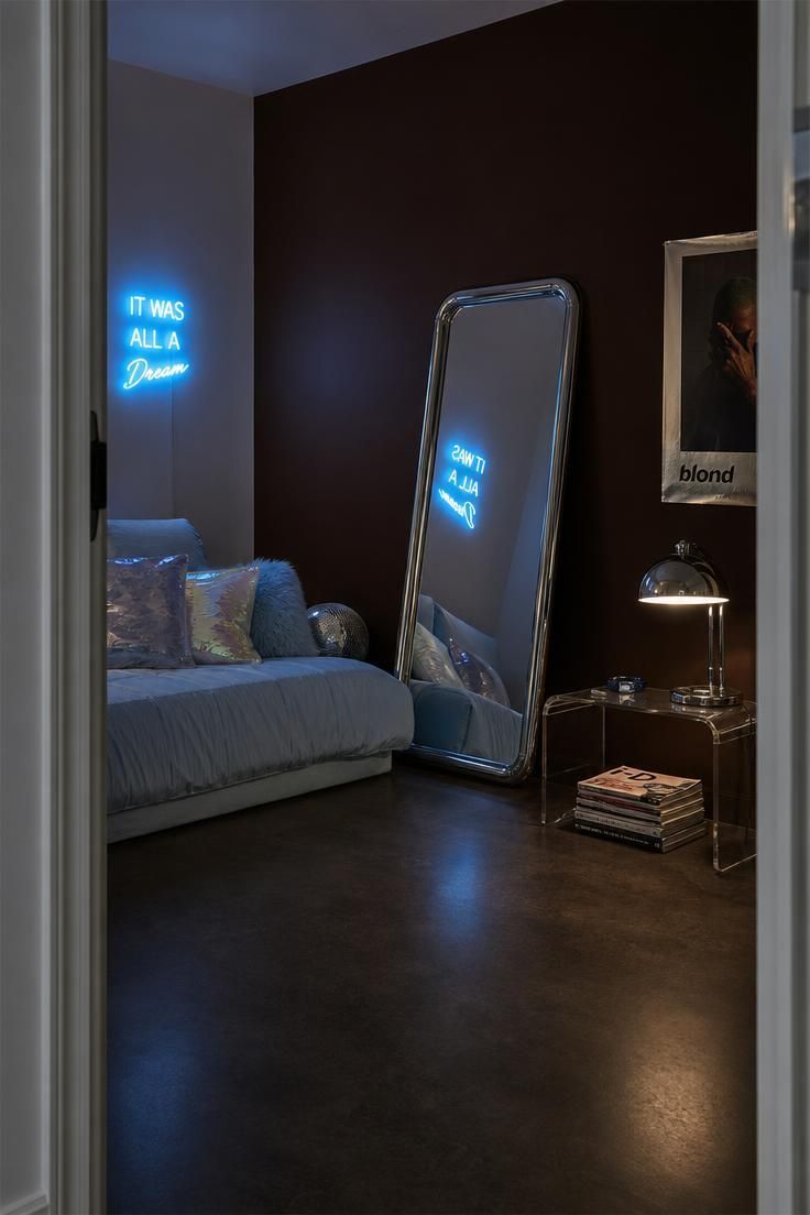 11 Cute Bedroom Ideas for Teens That Feel Super Cozy 11 Teen bedroom corner with chocolate-brown wall, chrome floor mirror, icy blue bedding, iridescent pillows, and a blue neon sign reflection.